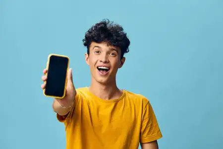 Веселый молодой человек с кудрявыми волосами держит смартфон, демонстрируя волнение и позитив