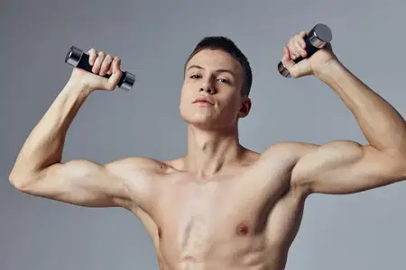Спортивный мужчина с гантелями в руках выполняет упражнение для мышц, демонстрируя силу