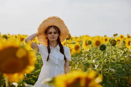 Девушка с косичками смотрит на подсолнуховое поле в сельской местности