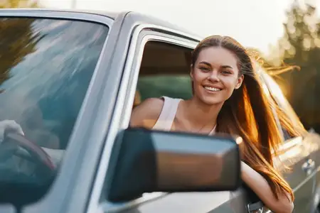 Веселая молодая женщина выглядывает из окна автомобиля, наслаждаясь радостью путешествия в солнечный день