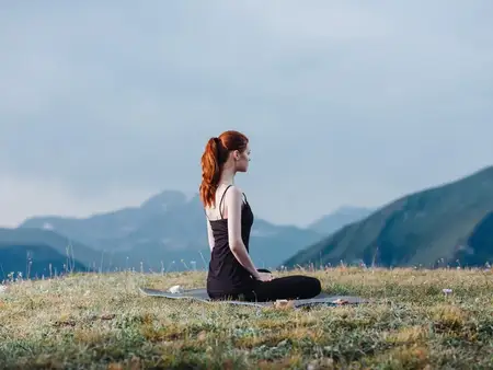 Стройная женщина в леггинсах и футболке занимается йогой на природе в горах