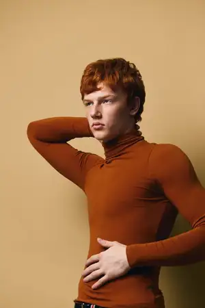 Рыжеволосый мужчина-модель в оранжевой водолазке стоит на однородном фоне