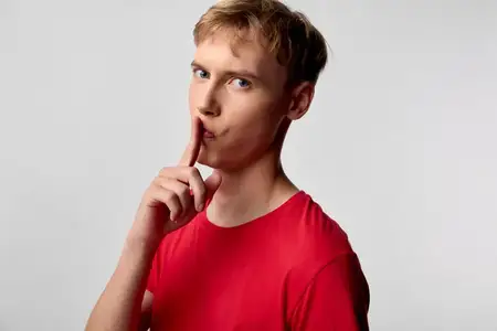 Мужчина в красной футболке, призывающий к тишине жестом «тсс» с пальцем у губ