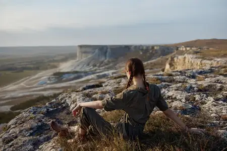 Женщина сидит на краю скалы, любуясь величественным видом на долину и горы