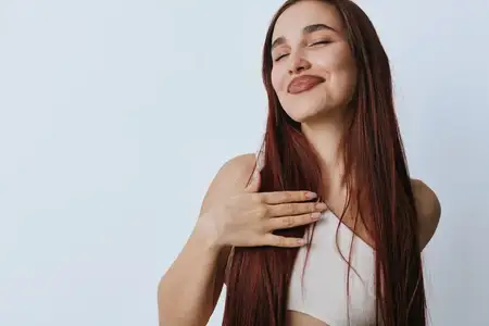 Молодая женщина с длинными каштановыми волосами выражает благодарность, положив руку на грудь и закрыв глаза