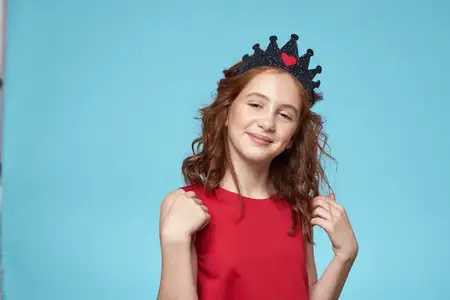 Девушка с кудрявыми волосами, в короне на голове и красном платье, ведет активный образ жизни на синем фоне