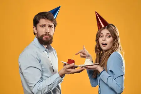 Мужчина и женщина в колпаках с тортом на жёлтом фоне, крупный план