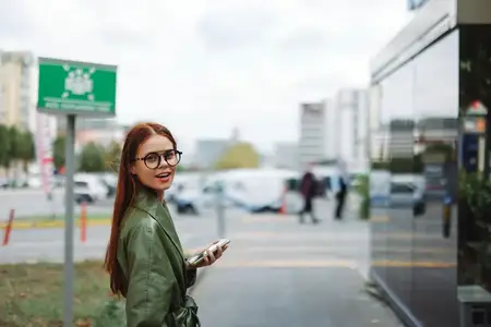 Женщина в стильной модной одежде идет по улице города, держа в руках телефон-навигатор с проложенным маршрутом