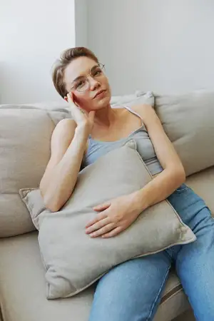 Женщина в очках сидит на диване и смотрит в камеру