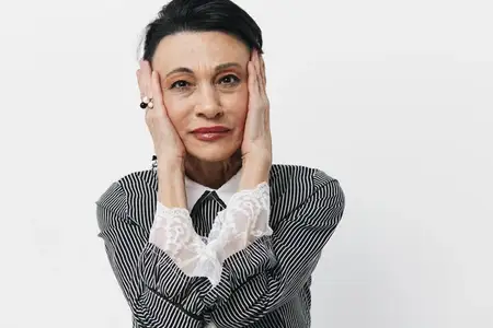 Портрет пожилой женщины, которая держит руки на лице, выражая шок и удивление, на фоне белого фона