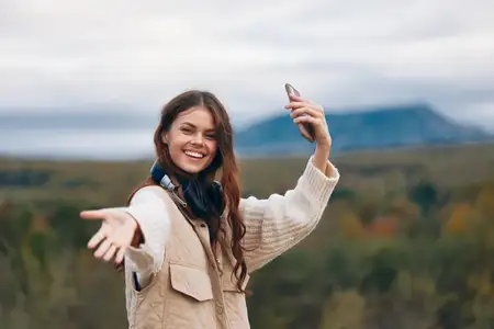 Женщина улыбается, наслаждаясь путешествием и технологиями на фоне величественных гор, ощущая горное блаженство