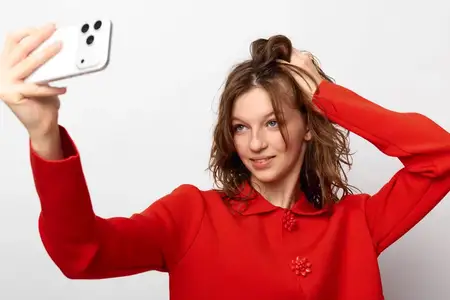 Улыбающаяся молодая женщина в красном свитере делает селфи на смартфон на белом фоне