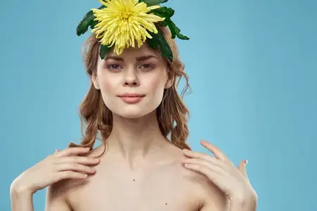 Женщина с желтым цветком на голове на голубом фоне, портрет с обнаженными плечами