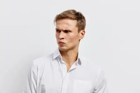 Скептически настроенный мужчина в белой рубашке смотрит в сторону с серьезным выражением лица на однотонном белом фоне