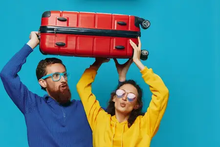 Женщина и мужчина улыбаются, держа в руках чемоданы — жёлтый и красный