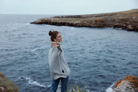 Женщина в сером свитере стоит на каменистом берегу