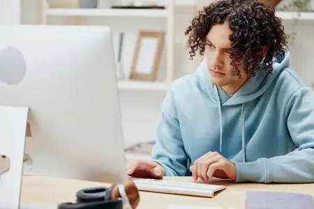 Молодой человек сидит перед компьютером, работая из дома в интерьере