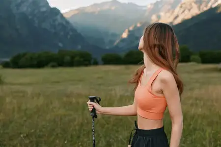 Женщина в спортивной одежде исследует широкий луг, сжимая походную палку, глядя вверх на суровые пики, передавая жизненную силу, исследование и активный отдых
