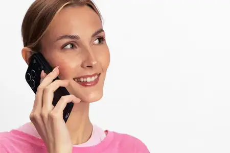 Молодая женщина в розовом свитере разговаривает по смартфону со счастливой улыбкой