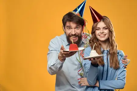 Мужчина и женщина в колпаках с именинным тортом на жёлтом фоне