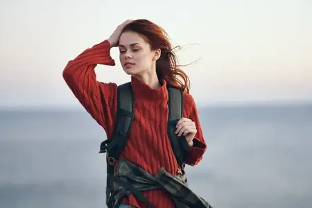 Женщина, женщина-туристка с рюкзаком возле моря в горах на природе, модель в красном свитере