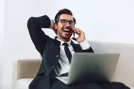 Молодой успешный работник улыбается, сидя в офисе, и работает за ноутбуком