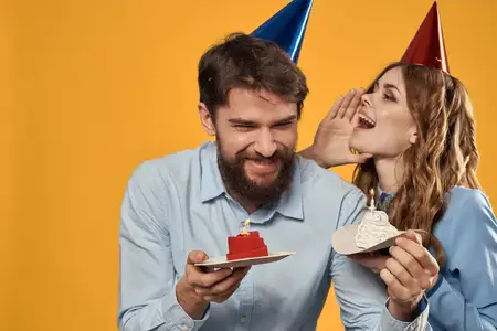 Мужчина и женщина на жёлтом фоне в колпаках, держащие в руках торт