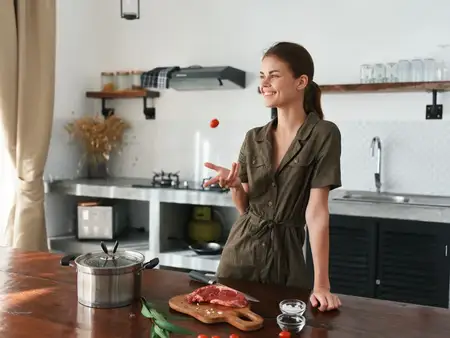Женщина улыбается на кухне, готовя обед из мяса, овощей и специй на деревянном столе на фоне стильной кухни