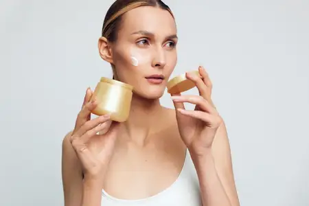 Портрет женщины, наносящей увлажняющий крем из золотой баночки