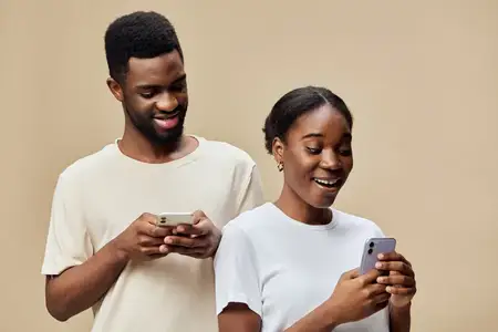 Счастливая африканская пара взаимодействует со своими смартфонами на фоне теплого бежевого фона, передавая темы технологий, связи и радости