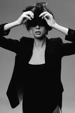 Черно-белый портрет модной женщины в пиджаке, с растрепанными волосами, закрывающими глаза, создающий загадочное и элегантное настроение на простом фоне