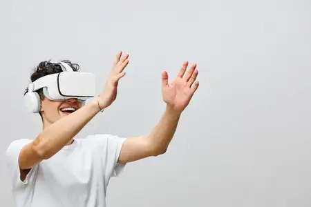 Радостный молодой человек в VR-очках взаимодействует с виртуальной средой, взволнованно размахивая руками
