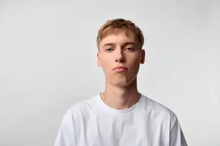 Студийный снимок мужчины в белой футболке на нейтральном фоне, выверенная поза и расслабленное настроение, простая одежда, ненавязчивое освещение, подходит для проектов на тему образа жизни, моды…