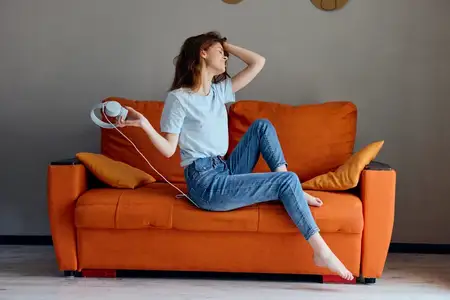 Улыбающаяся девушка на оранжевом диване слушает музыку в наушниках