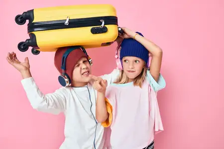 Портрет девочки и мальчика с желтым чемоданом в руках на изолированном фоне