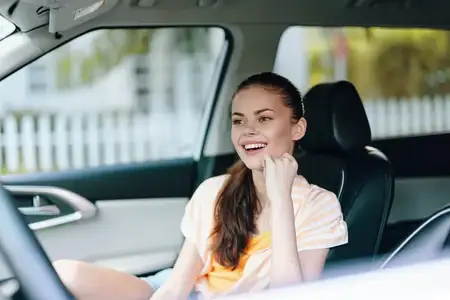 Молодая женщина сидит на водительском сиденье автомобиля, радостно улыбаясь и наслаждаясь моментом
