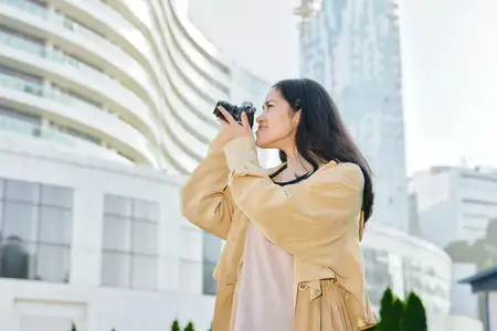 Уличная сцена: женщина с фотоаппаратом среди городской архитектуры в стильном пальто при дневном свете