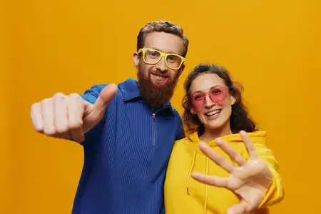 Мужчина и женщина, пара, весело и с улыбкой позируют, слегка наклонившись, в очках на жёлтом фоне