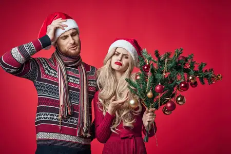 Мужчина с рождественской елкой в руках стоит рядом с женщиной, передавая эмоции праздничного украшения