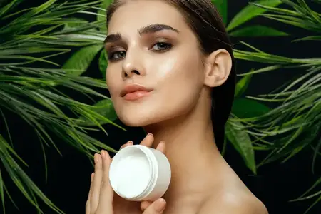Женщина с баночкой крема рядом с зелеными листьями пальмовых кустов