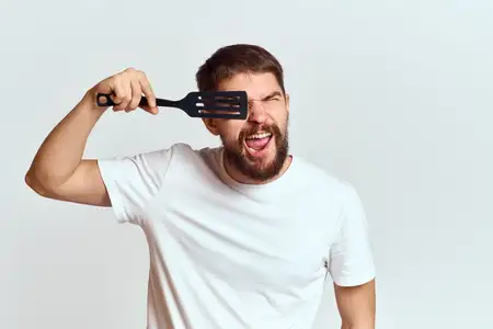 Мужчина с кухонной лопаткой в белой футболке, крупный план, обрезанный вид, эмоции, жестикулирует рукой