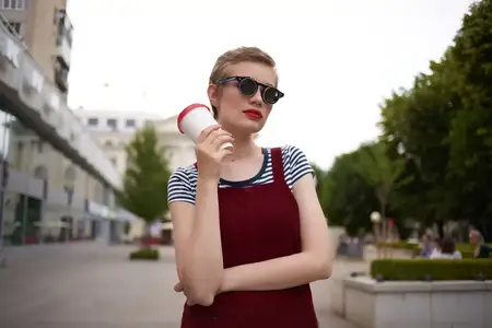 Женщина с короткими волосами на улице в солнцезащитных очках с напитком