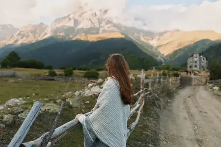 На outdoor-сцене женщина обозревает долину и альпийскую сельскую местность, запечатлевая безмятежный момент образа жизни при естественном освещении и обширных горных пейзажах