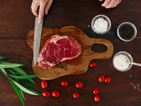 Женщина с ножом в руке нарезает свежее мясо стейка для жарки на кухне
