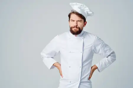 Бородатый мужчина в рабочей униформе, его профессия связана с кухней, на светлом фоне