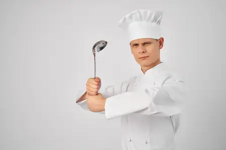 Эмоциональный шеф-повар-мужчина с кухонными принадлежностями работает на кухне ресторана, готовит