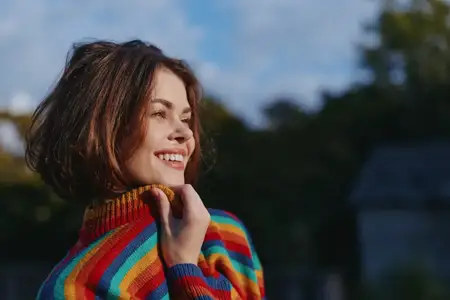 Улыбающаяся женщина в полосатом свитере с короткой стрижкой позирует на улице в парке