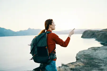 Женщина на закате у моря в горах, на плечах у неё рюкзак