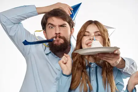Энергичные мужчина и женщина с тортом и в праздничных колпаках отмечают день рождения на светлом фоне