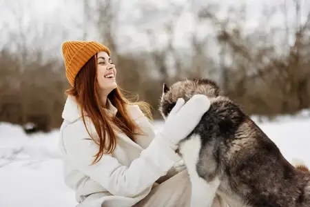 Молодая женщина играет в снегу с собакой
